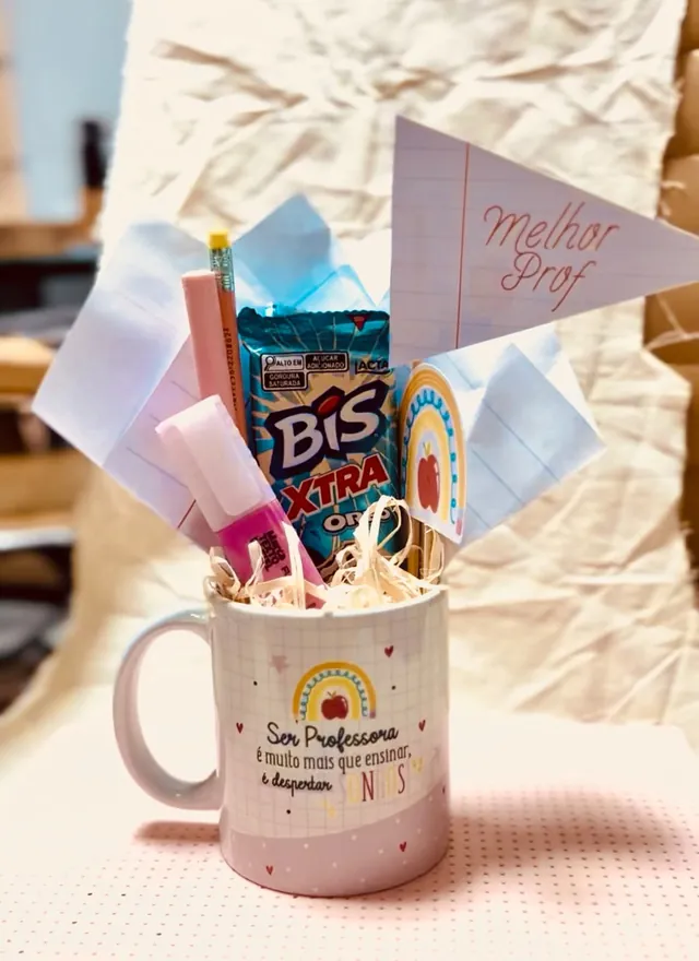 Caneca branca quadriculada com arco-íris, maçã e a frase Ser professora é muito mais que ensinar, é despertar sonhos, montada como kit com bandeirinha Melhor Prof, tag de arco-íris, lápis, marca-texto e chocolate.